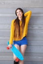 Smiling young woman leaning against wall with skateboard Royalty Free Stock Photo