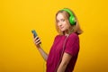 Smiling young woman listens music in headphones holds mobile phone chooses song from playlist Royalty Free Stock Photo