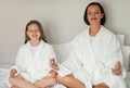 Smiling young woman and little caucasian girl in bathrobe with closed eyes, meditation, resting on white bed Royalty Free Stock Photo