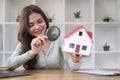 Smiling young woman looking at house model with magnifying glass. Real estate appraisal, land valuation and house selection Royalty Free Stock Photo