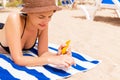 Smiling young woman is lying on striped towel on the sand at the beach and applying sun cream on her hand Royalty Free Stock Photo