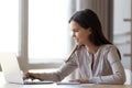 Smiling young woman making notes using laptop