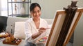 Smiling young woman painting picture on canvas with oil paints in bright cozy living room. Art, creative hobby and Royalty Free Stock Photo