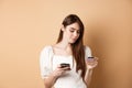 Smiling young woman paying online, looking at credit card and making purchase on mobile phone, shopping in internet