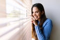 Happy young woman looking through venetian blinds on window Royalty Free Stock Photo