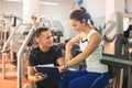 Smiling young woman with personal trainer and exercise plan on clipboard at gym. Royalty Free Stock Photo