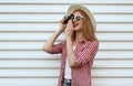 Smiling young woman photographer with vintage film camera wearing summer round straw hat, checkered shirt on white wall Royalty Free Stock Photo