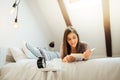 Smiling young woman reading book and enjoying warm coffee in sunny apartment.Relaxation in bed.Sunny light warm home.Hygge