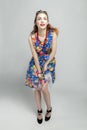 Smiling young woman. Red-haired girl in a dress with a floral print, red beads and sunglasses. Gray background. Vertical. Full Royalty Free Stock Photo