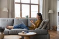 Smiling young woman holds smartphone relaxing on sofa with laptop Royalty Free Stock Photo