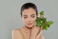 Smiling young woman with shiny perfect facial skin and bare shoulder holding spring flowers and green leaves. Spa beauty model Royalty Free Stock Photo