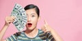 Smiling young woman showing thumb up, holding fan of money in dollar banknotes, cash money isolated on pink pastel background Royalty Free Stock Photo