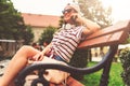 Smiling young woman sitting on a bench in the summer using smart phone Royalty Free Stock Photo