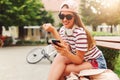 Smiling young woman sitting on a bench in the summer using smart phone Royalty Free Stock Photo