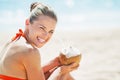 Smiling young woman sitting with coconut on beach Royalty Free Stock Photo