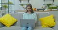 Smiling young woman sitting on couch using laptop notebook looking at screen typing message, happy lady chatting on Royalty Free Stock Photo