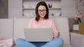 Smiling asian woman sitting on sofa using laptop computer looking at screen typing message, mixed race lady chatting on Royalty Free Stock Photo