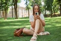 Smiling young woman sitting on green grass using mobile phone in park browsing internet having free time enjoyinh social network Royalty Free Stock Photo