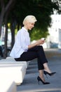 Smiling young woman sitting outside reading text message Royalty Free Stock Photo