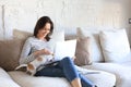 Smiling woman sitting on sofa with laptop computer, little dog playing near Royalty Free Stock Photo