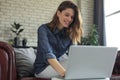 Smiling young woman sitting on sofa with laptop computer and chating with friends