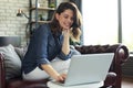 Smiling young woman sitting on sofa with laptop computer and chating with friends