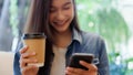 Smiling young woman sitting at table with hot cup of coffee and using mobile phone Royalty Free Stock Photo