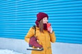 smiling young woman with skates over her shoulder and a paper cup of coffee near the bright blue wall of the ice arena Royalty Free Stock Photo