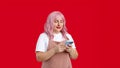 Smiling young woman in apron with smart phone posing isolated on red background, studio portrait. Cute beautiful woman Royalty Free Stock Photo