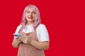 Smiling young woman in apron with smart phone posing isolated on red background, studio portrait. Cute beautiful woman Royalty Free Stock Photo