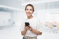 Smiling young woman with smartphone in casual clothes in office Royalty Free Stock Photo