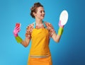 Smiling young woman with sponge looking at washed dish on blue