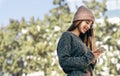 Smiling young woman standing outdoors chatting with her friend on smart phone. Side view image of pretty female dressed in knitted Royalty Free Stock Photo