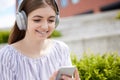Smiling Young Woman Student On College Campus Streams Music From Mobile Phone To Wireless Headphones Royalty Free Stock Photo