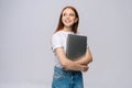 Smiling young woman student holding laptop computer and looking away on isolated gray background. Royalty Free Stock Photo