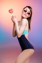 Smiling young woman in sunglasses and swimsuit holding heart-shaped candy Royalty Free Stock Photo