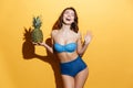 Smiling young woman in swimwear holding pineapple.