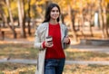 Smiling young woman with takeout coffee and tablet computer on walk at park on cool fall day