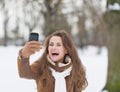 Smiling young woman taking photo using cell phone in winter park Royalty Free Stock Photo