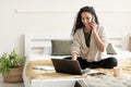 Smiling young woman talking on cellphone, using laptop, sitting on bed at home, empty space Royalty Free Stock Photo