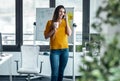 Smiling young woman talking with her mobile phone while standing next to the window in the office at home Royalty Free Stock Photo