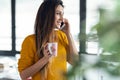 Smiling young woman talking with her mobile phone while standing next to the window in the office at home Royalty Free Stock Photo