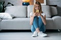 Smiling young woman using her mobile phone while sitting on the floor in the living room at home Royalty Free Stock Photo