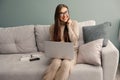 Smiling young woman using laptop, sitting on couch at home, beautiful girl shopping or chatting online in social network, Royalty Free Stock Photo