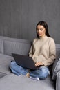 Smiling young woman using laptop, sitting on couch at home. Beautiful girl shopping or chatting online in social network, having Royalty Free Stock Photo