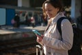 Smiling young woman using mobile phone while waiting train, on the platform of a railway station Royalty Free Stock Photo