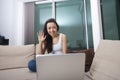 Smiling young woman waving in front of laptop on sofa Royalty Free Stock Photo