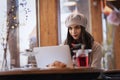 Smiling young woman wearing beret had and scarf while using her laptop at the cafe