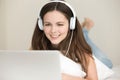 Smiling young woman wearing headphones lying on bed using laptop