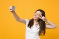 Smiling young woman in white casual clothes showing victory sign, doing selfie shot on mobile phone  on bright Royalty Free Stock Photo